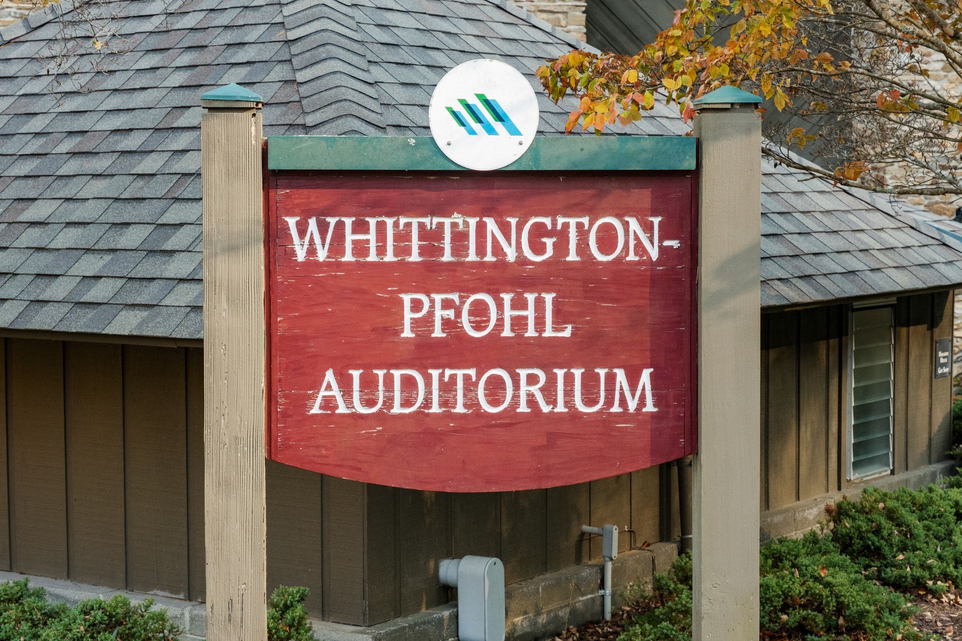 Wooden sign reading “Whittington-Pfohl Auditorium” in front of a building