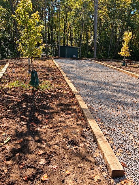 Gravel driveway under construction beside a dirt path and young trees in a wooded area