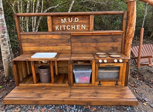 Wooden outdoor mud kitchen playset with sink, stove, storage bins, and “MUD KITCHEN” sign
