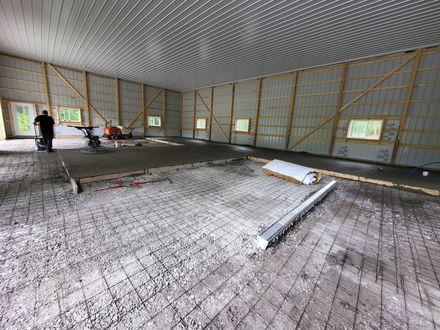 Interior view of a building under construction, showing a metal-paneled ceiling, gravel floor with rebar, and concrete slab.