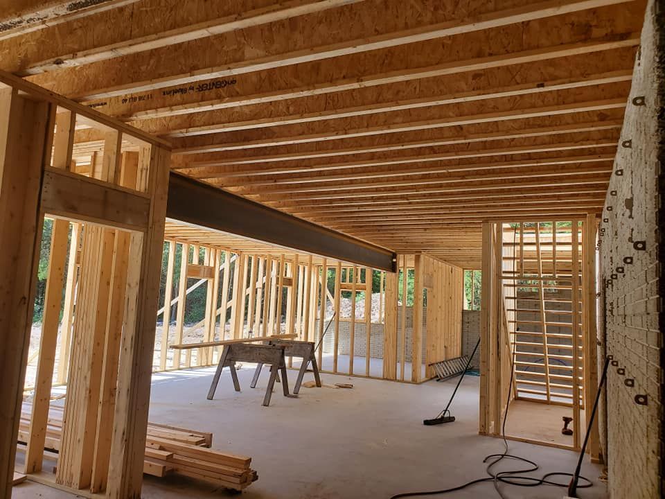 Interior view of a residential construction site featuring wooden framing, exposed floor joists, and a steel support beam.