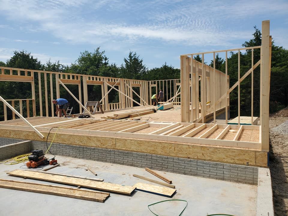 Construction workers frame the wooden walls and floor joists of a house under construction on a concrete foundation.