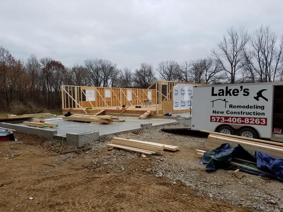 Wood framing for a house under construction on a concrete foundation, next to a trailer for Lake’s Remodeling.