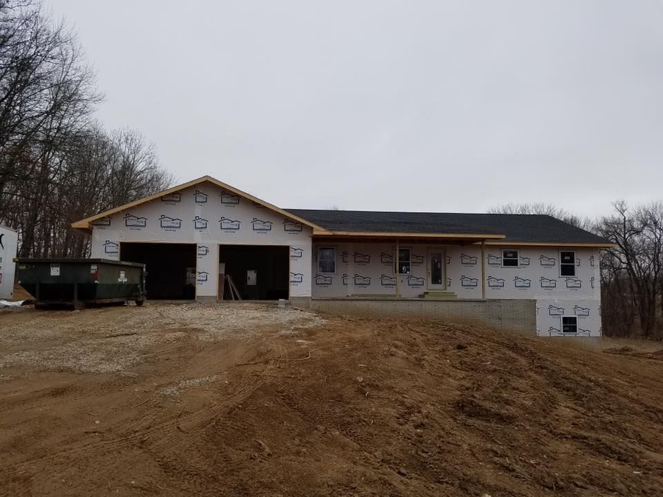 A new single-story house under construction with white exterior house wrap, a dark roof, and an attached two-car garage.