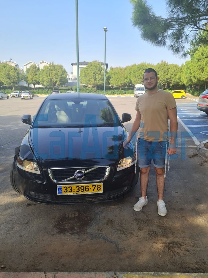 גבר עם קביים עומד מול מכונית וולוו בחניון.