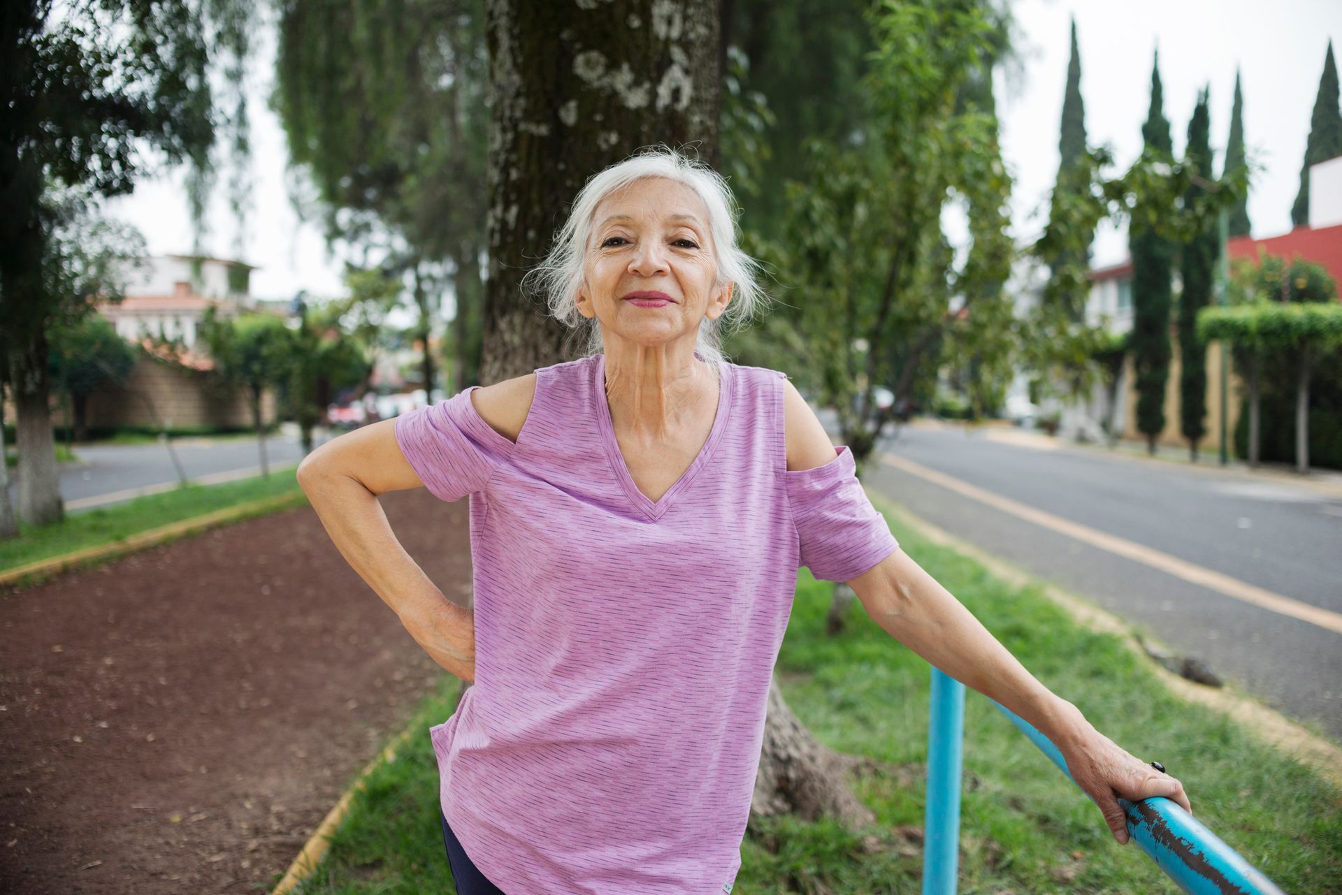 An older woman in a pink shirt, poses outside.