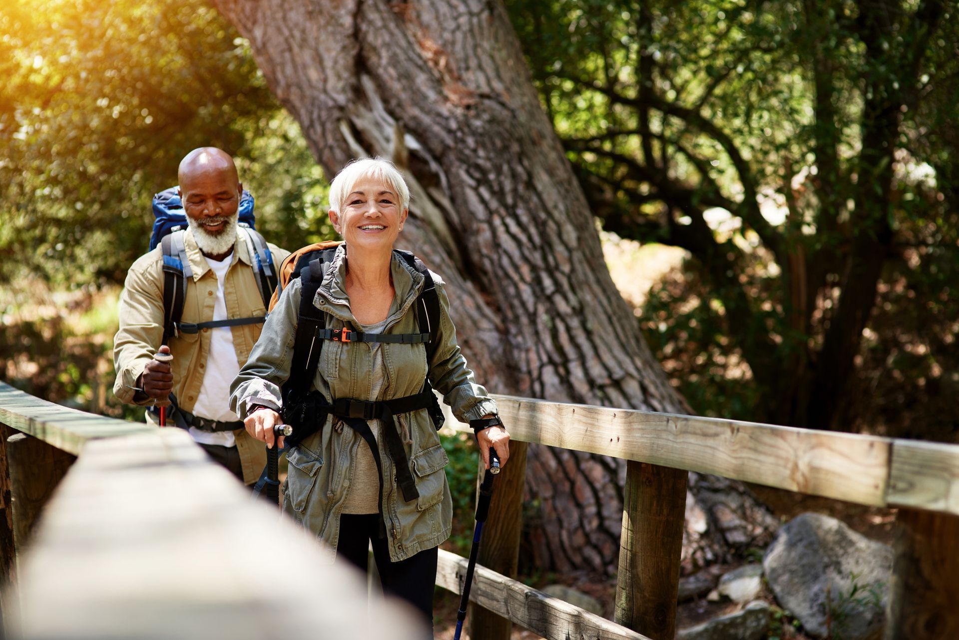 Two people hike on a wooden bridge in a forest.