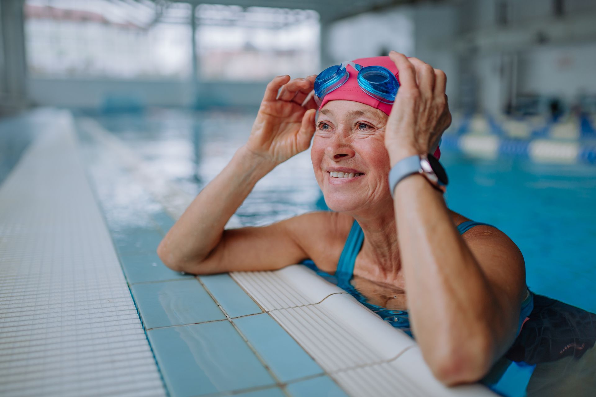Woman in pool with pink swim cap and goggles smiles.