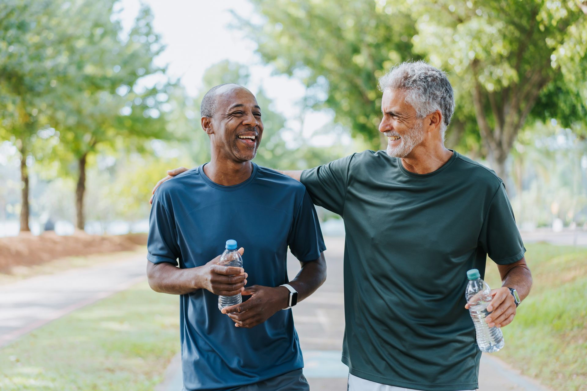 Two older men, smiling, walking on path in park.