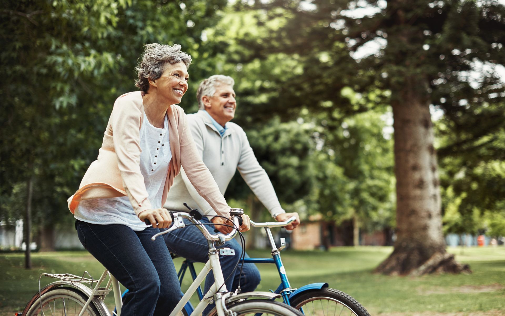 Elderly couple smiling and riding bicycles in a park.