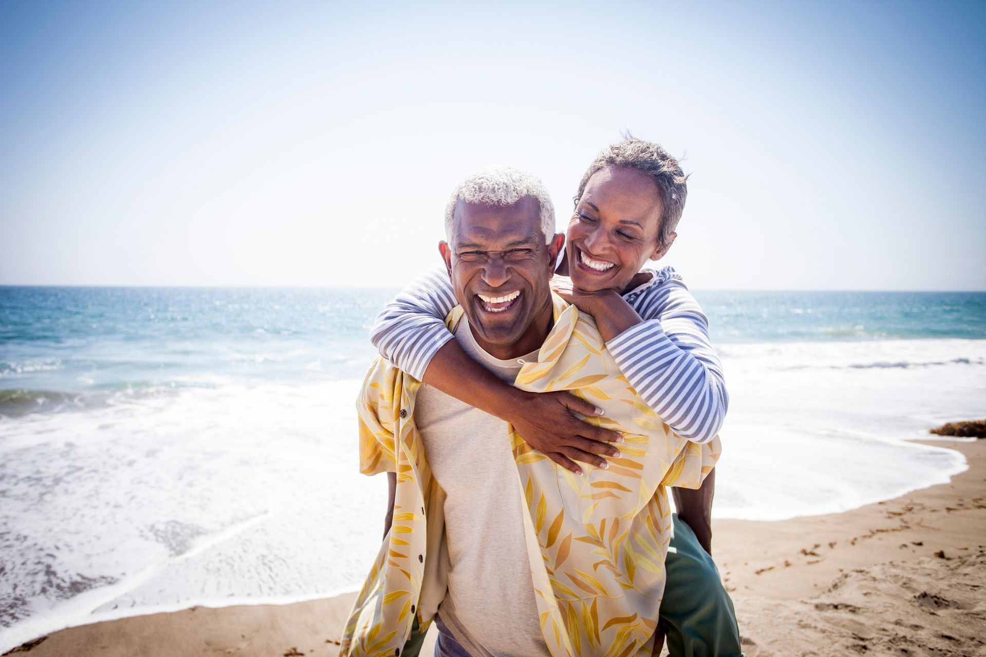 Mature couple laughing on beach, woman piggybacking man.