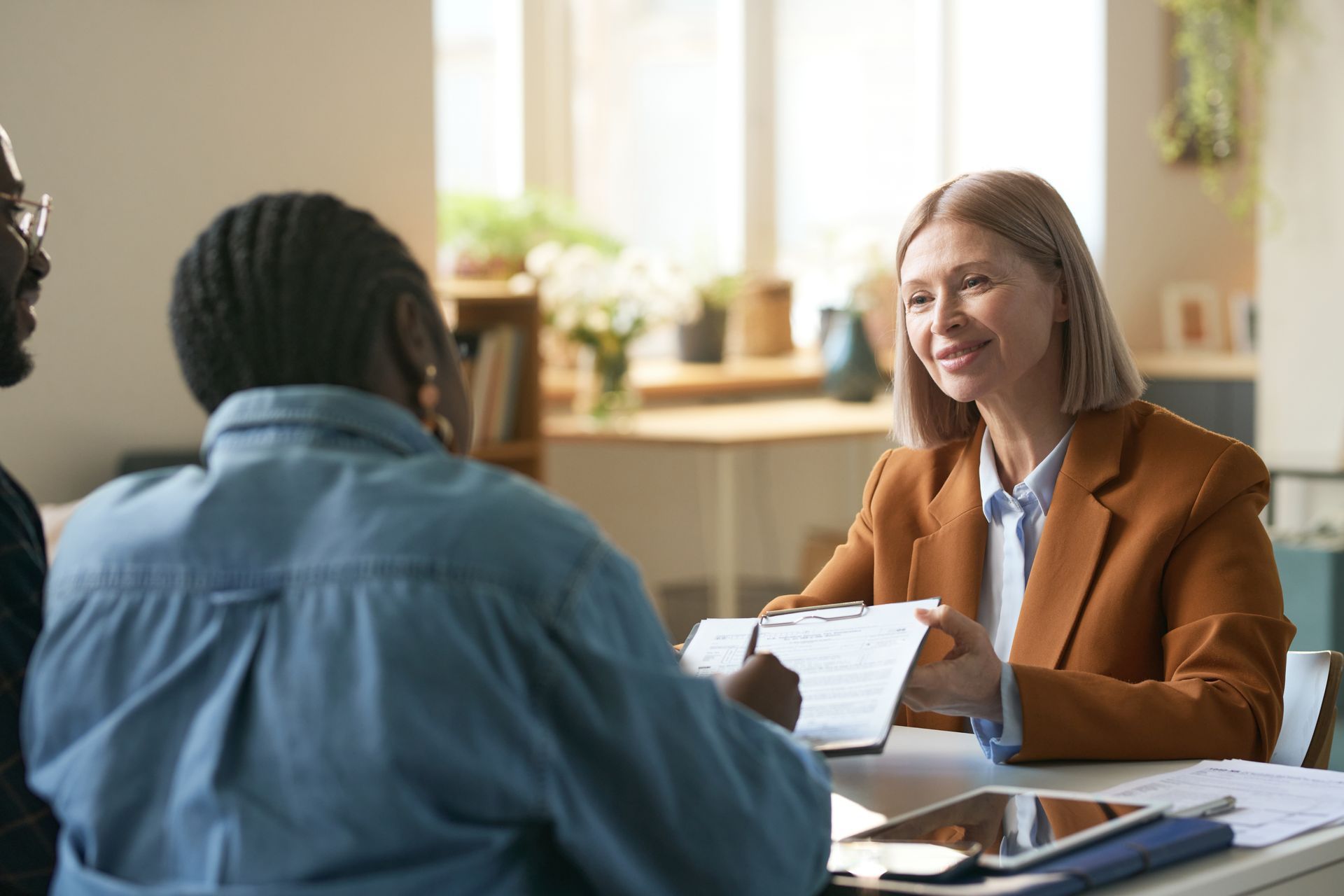 Two people talking at a table in a bright office, one holding papers and smiling. Two people talking at a table in a bright office, one holding papers and smiling.