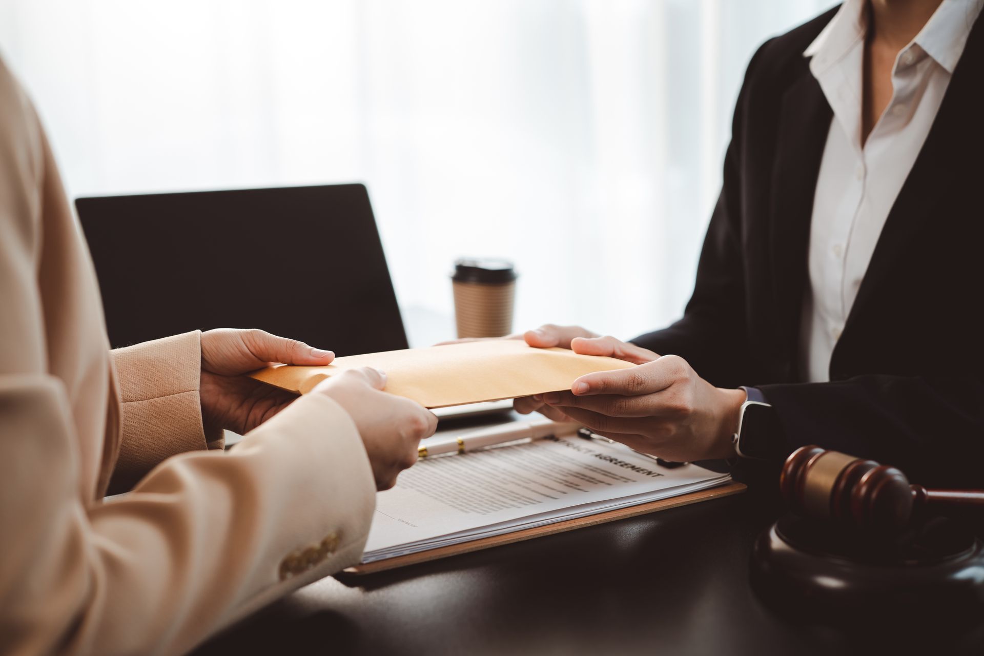 Two people exchange a folder across a desk in an office meeting Two people exchange a folder across a desk in an office meeting