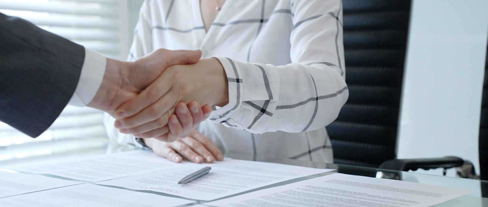 Business handshake over documents on a desk in a bright office