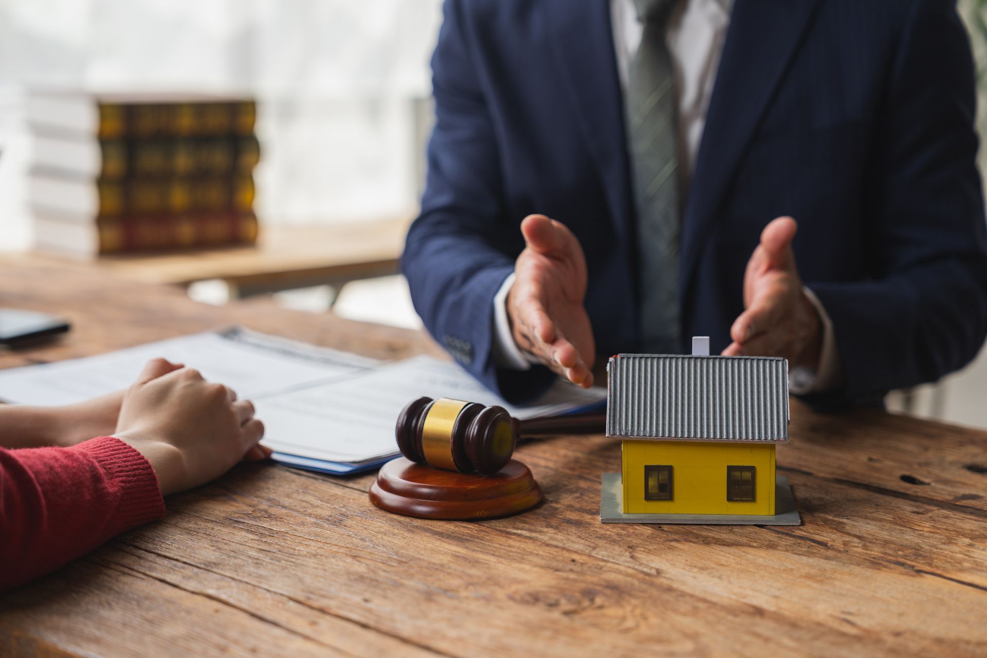 Hands gesturing over a small house model and gavel on a table, with papers in a legal setting