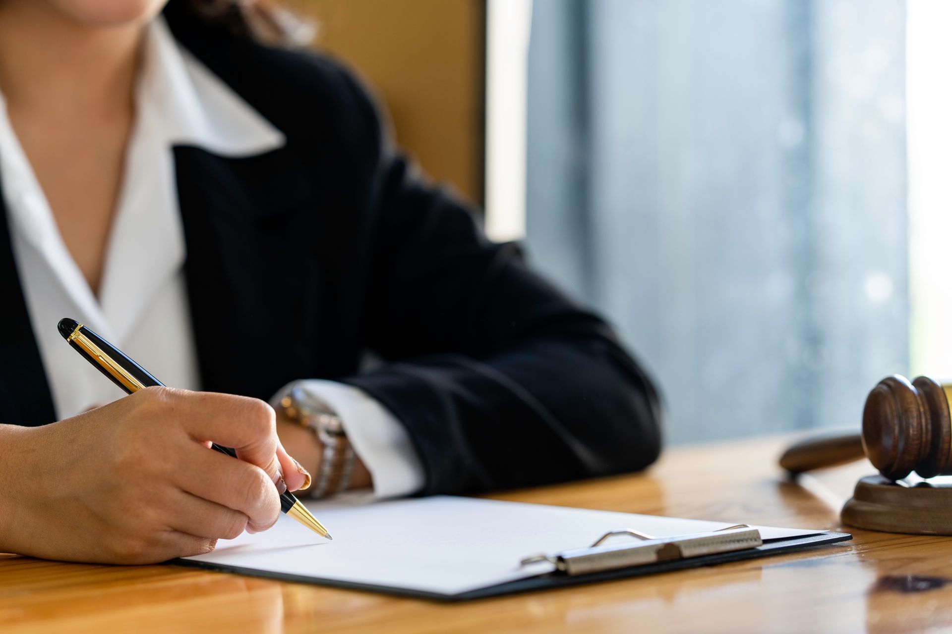 Person writing on paper at a desk with a gavel nearby