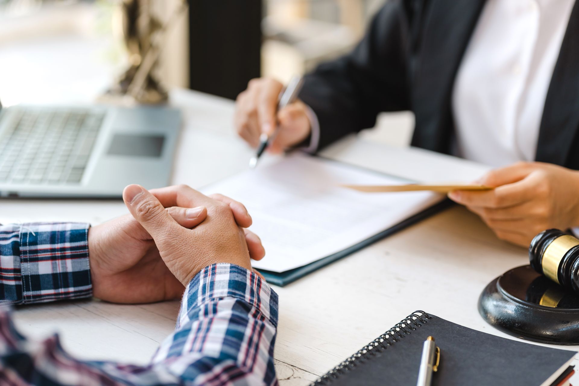 Hands clasped across a desk during a business meeting, with paperwork, laptop, and a judge’s gavel visible. Hands clasped across a desk during a business meeting, with paperwork, laptop, and a judge’s gavel visible.