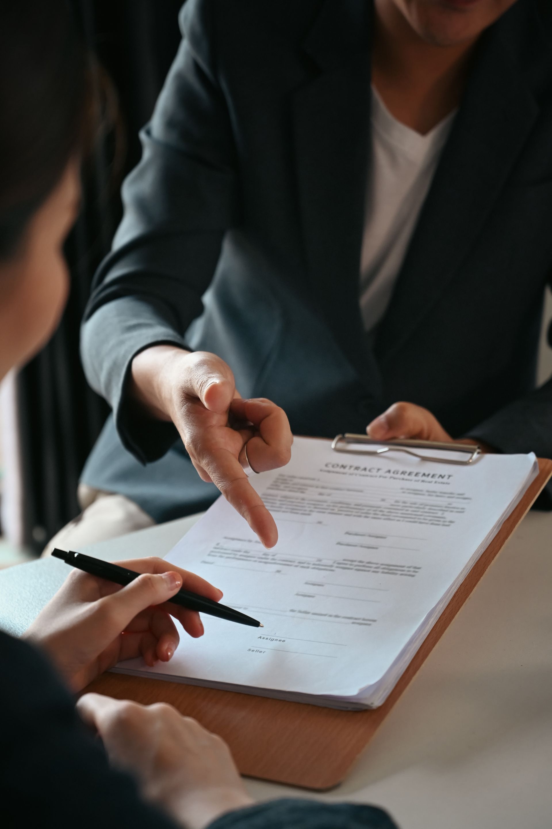 Two people review a document on a clipboard, with one pointing and the other holding a pen. Two people review a document on a clipboard, with one pointing and the other holding a pen.