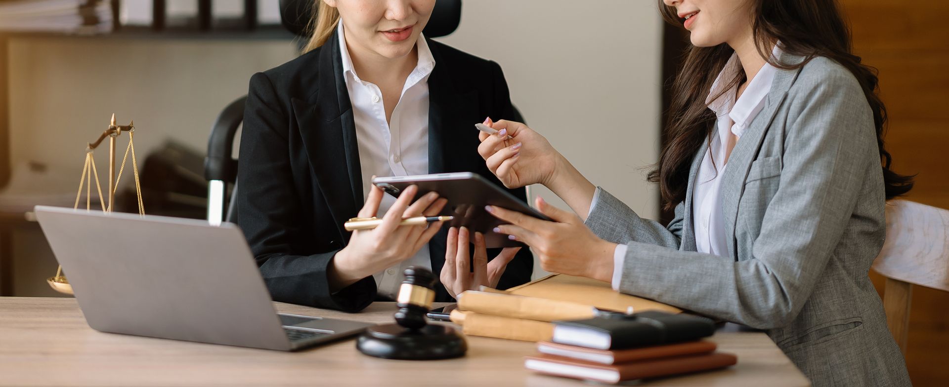 Two coworkers discussing a tablet at a desk with a laptop and notebooks in an office