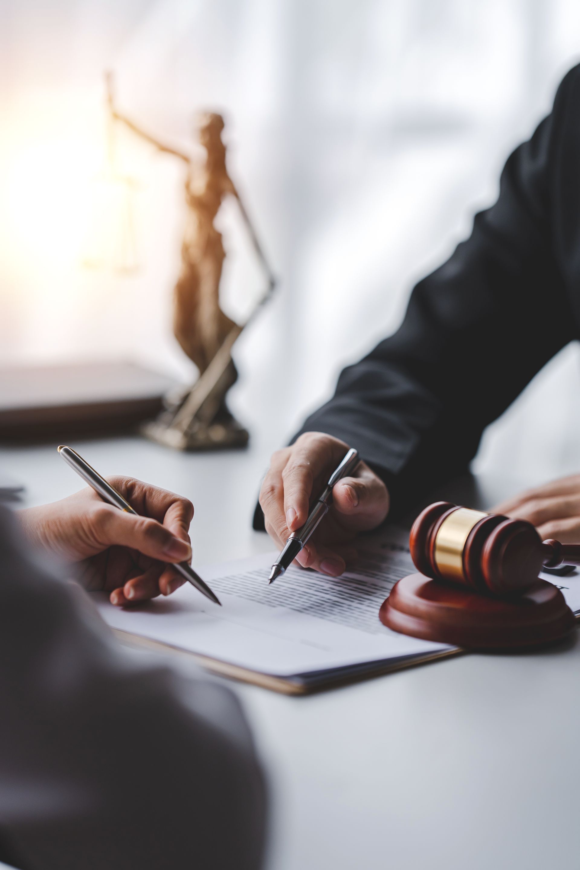 Hands signing legal documents beside a gavel in a courtroom-like office setting Hands signing legal documents beside a gavel in a courtroom-like office setting