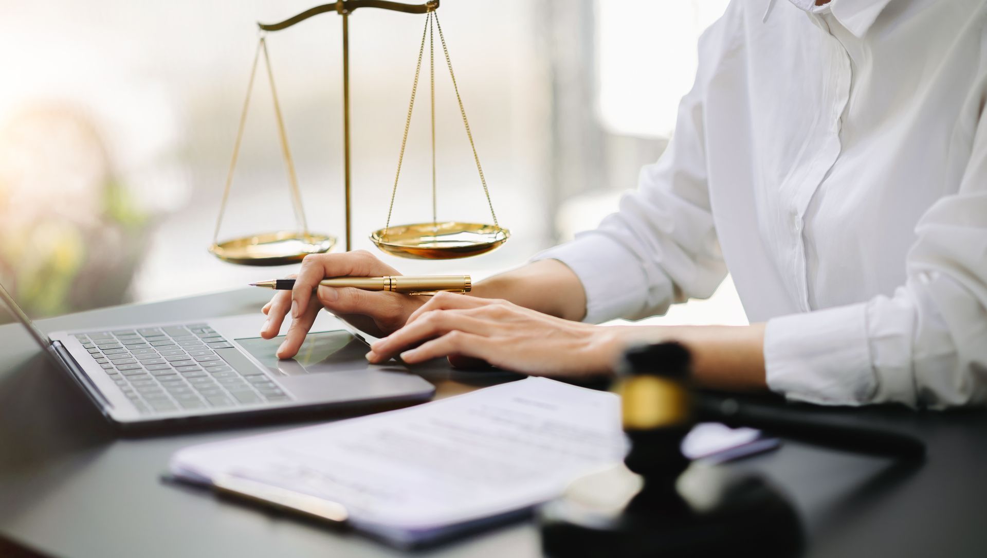 Lawyer using laptop and notebook beside a golden scales of justice on a desk
