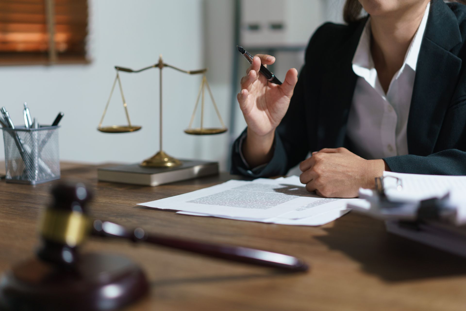Lawyer in a suit signing documents at a desk with a balance scale and gavel in the background Lawyer in a suit signing documents at a desk with a balance scale and gavel in the background