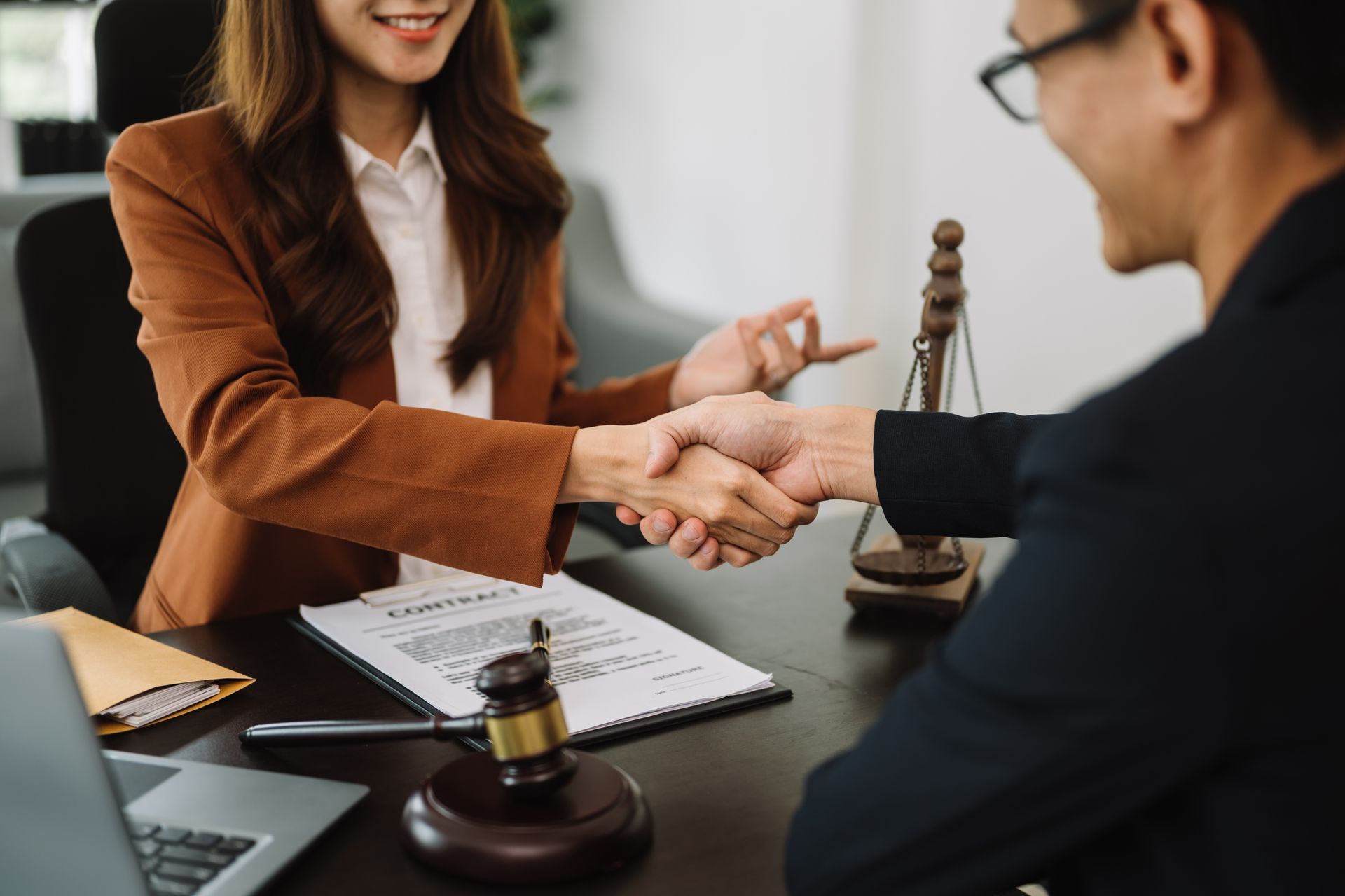 Business handshake across a desk in a law office, with a gavel and paperwork visible.