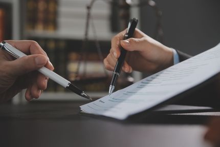 Two hands signing a document with pens at a desk