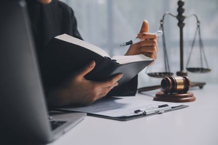 Lawyer holding a folder beside a gavel and scales of justice on a desk Lawyer holding a folder beside a gavel and scales of justice on a desk