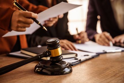 Gavel on a table in a courtroom as people review papers and documents nearby Gavel on a table in a courtroom as people review papers and documents nearby