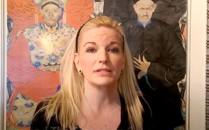 Woman speaking in front of two colorful framed portraits on a wall Woman speaking in front of two colorful framed portraits on a wall