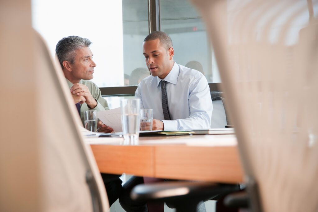 Two people in business attire talking at a conference table in a bright office.