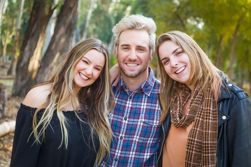 Three smiling friends posing outdoors in casual clothes, with trees in the background
