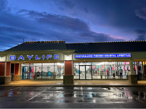 Baylife store exterior lit up at dusk, selling coastal lifestyle apparel