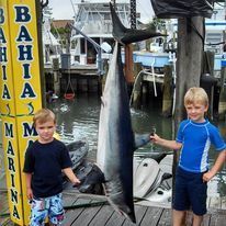 Two young boys are standing next to a large shark on a dock.