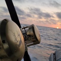 A close up of a fishing reel on a boat in the ocean at sunset.