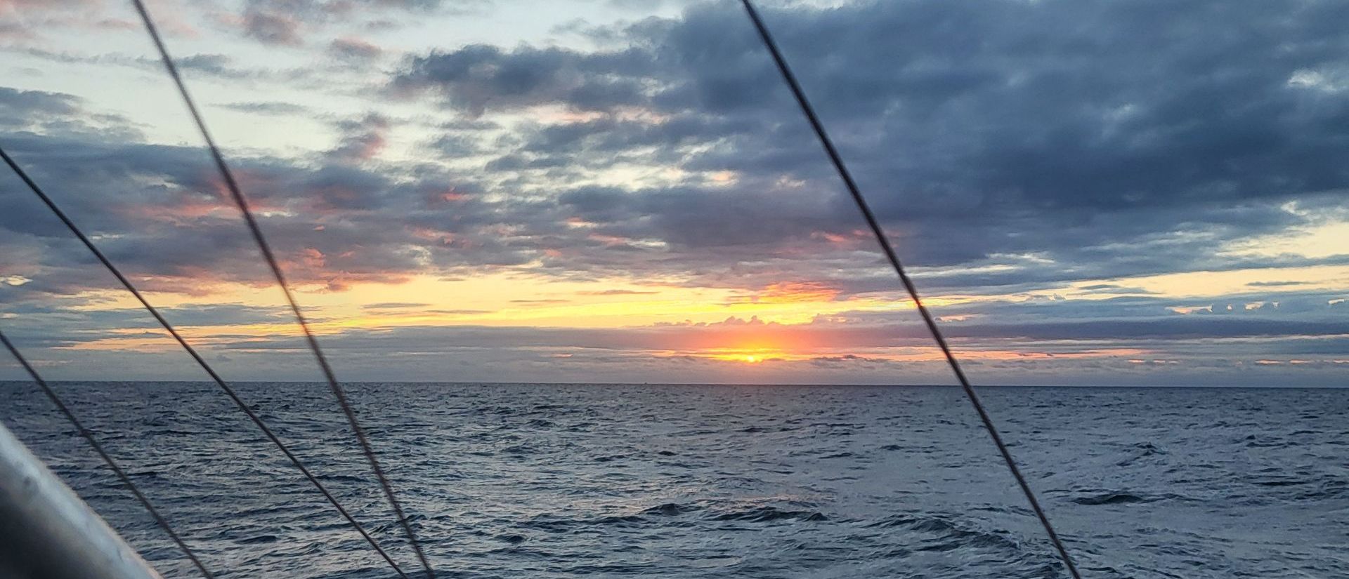 A sunset over a body of water with a sailboat in the foreground