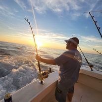 A man is fishing on a boat in the ocean at sunset.