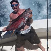 A shirtless man is holding a large fish on a boat.