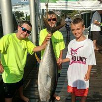 A group of young boys are standing on a dock holding a large fish.