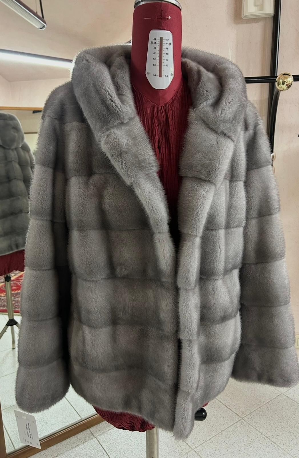 Cappotto grigio in pelliccia sintetica appeso a un manichino rosso in un negozio di abbigliamento o in uno studio.