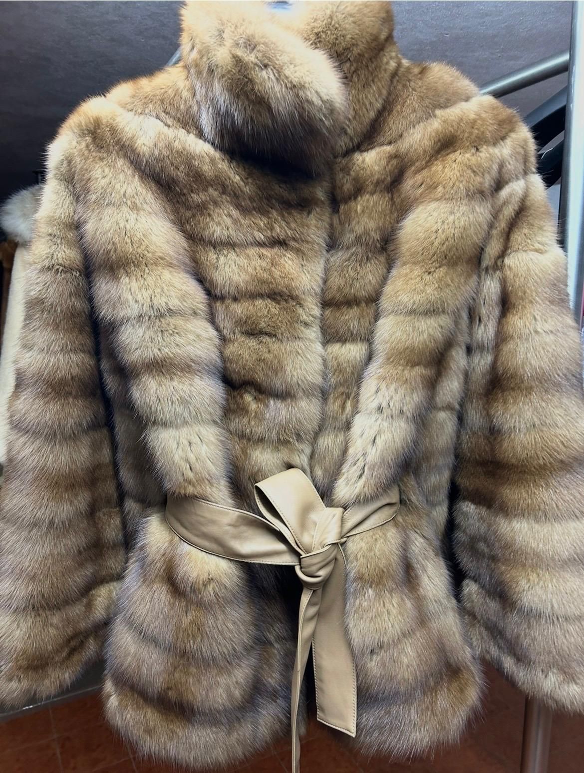Cappotto di pelliccia a righe con cintura in vita, appeso a una gruccia.