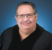 Headshot of a smiling person wearing glasses and a black judicial robe against a blue background.