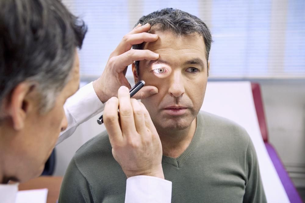 A Doctor is Examining a Man's Eye With a Magnifying Glass — Michael Chu Optometrist in Cairns North, QLD