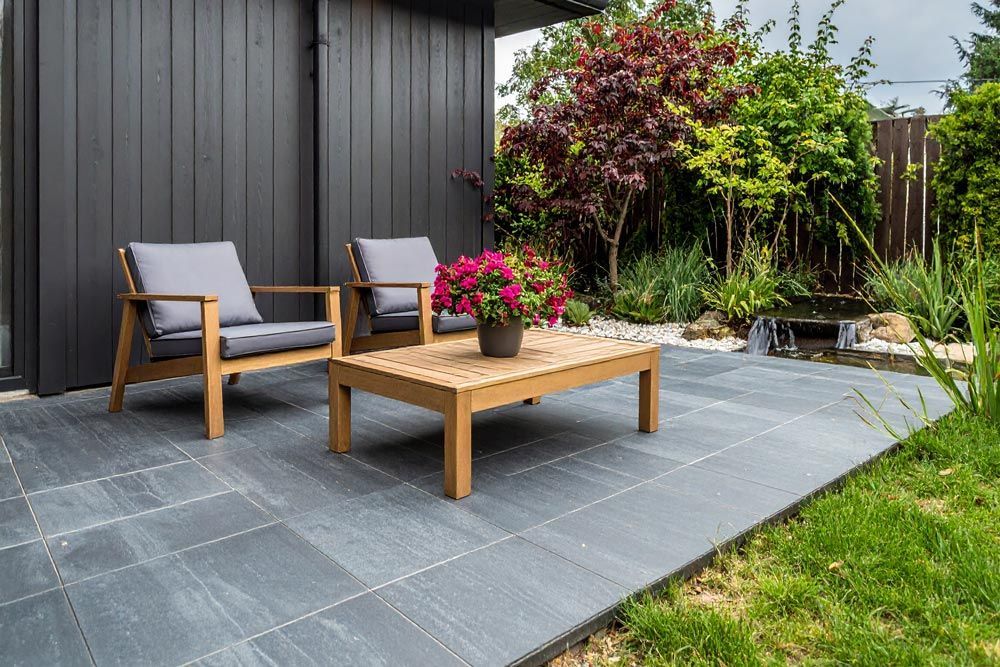 Patio with two gray cushioned chairs and a coffee table, next to a garden with green grass.