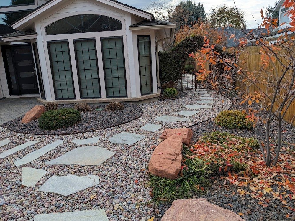 Curved stone walkway leading to a house entry with landscaping, gravel, and autumn foliage