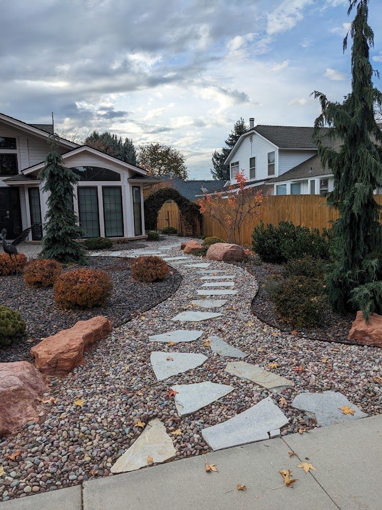 Rock garden path with stepping stones leading to a house, lined with shrubs and gravel under a cloudy sky
