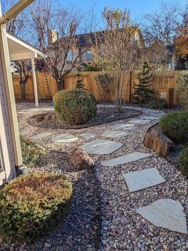 Stepping-stone path through a landscaped backyard with gravel, shrubs, and wooden fencing.