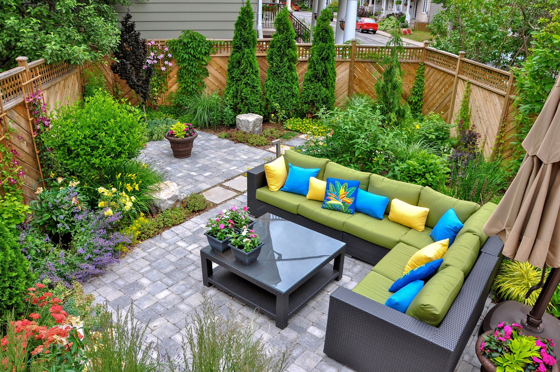 Outdoor patio with green sectional sofa, brick patio, lush greenery, and wood fence.