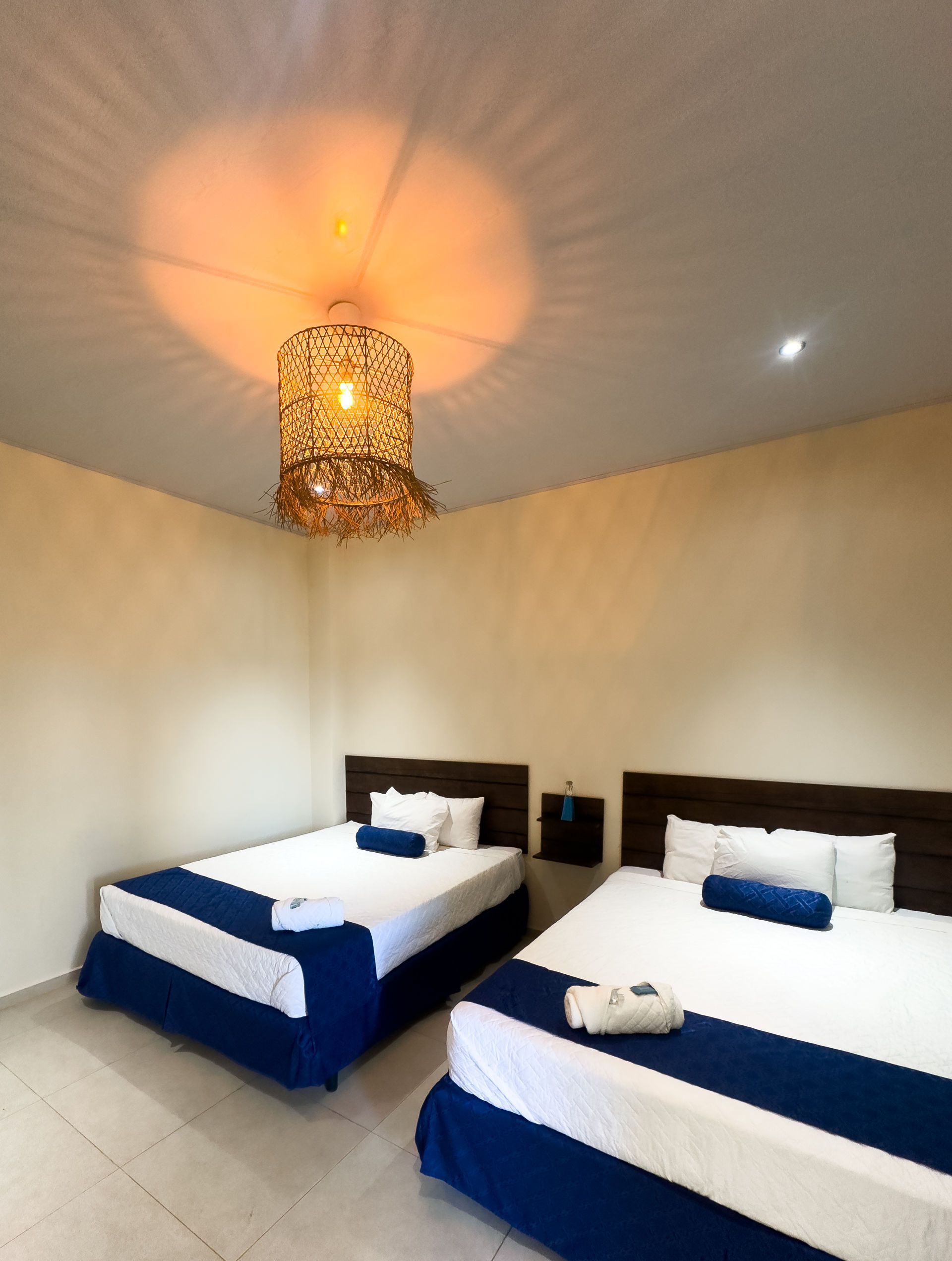 Dos camas en una habitación con detalles azules, una lámpara decorativa y paredes de color claro.